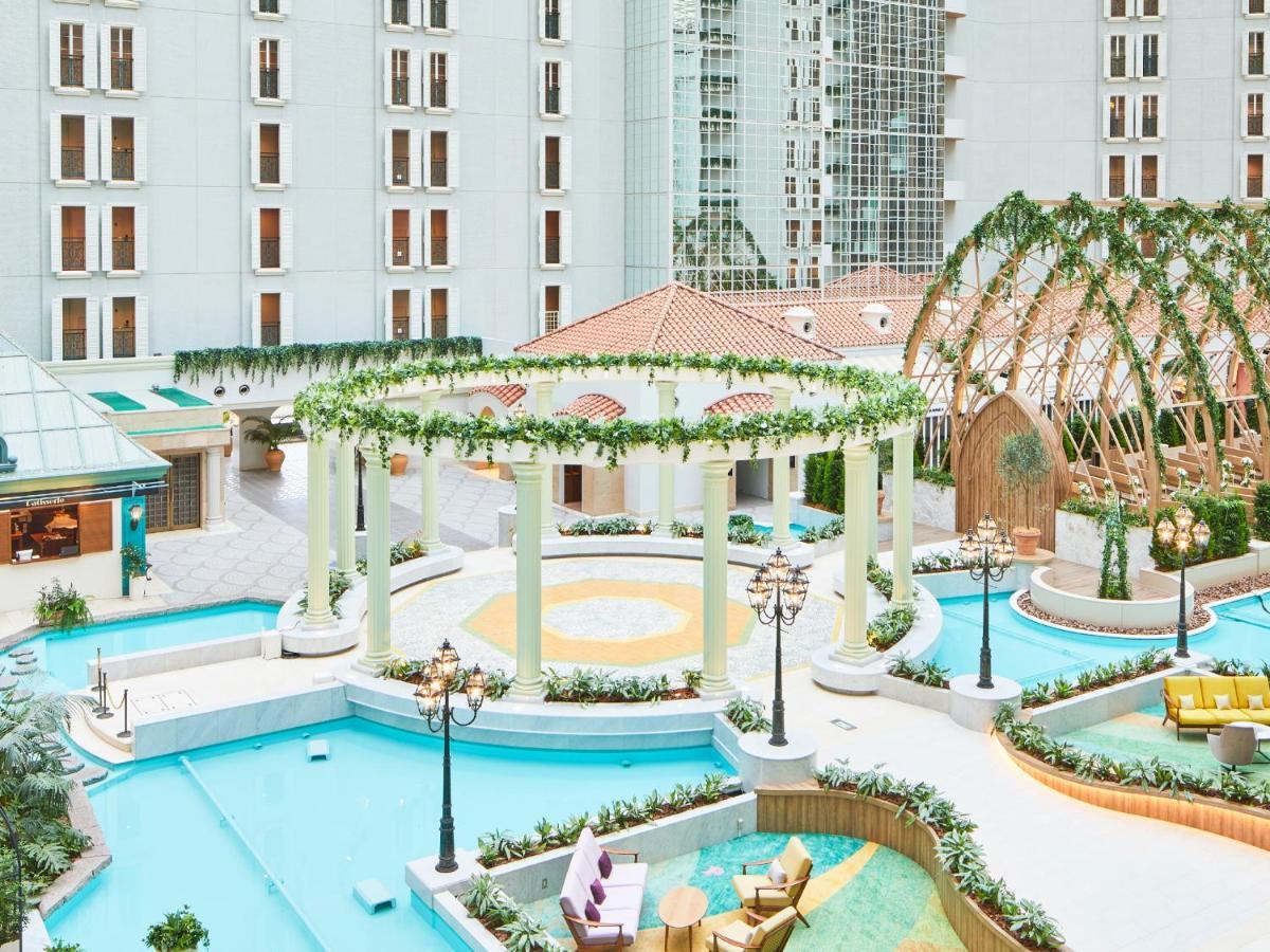 Grand Nikko Tokyo Bay Maihama Hotel Urayasu Eksteriør billede The photo shows a beautifully landscaped outdoor area, likely part of a resort or hotel. It features a central circular structure supported by white columns, decorated with greenery. Surrounding this structure are several swimming pools or water feat