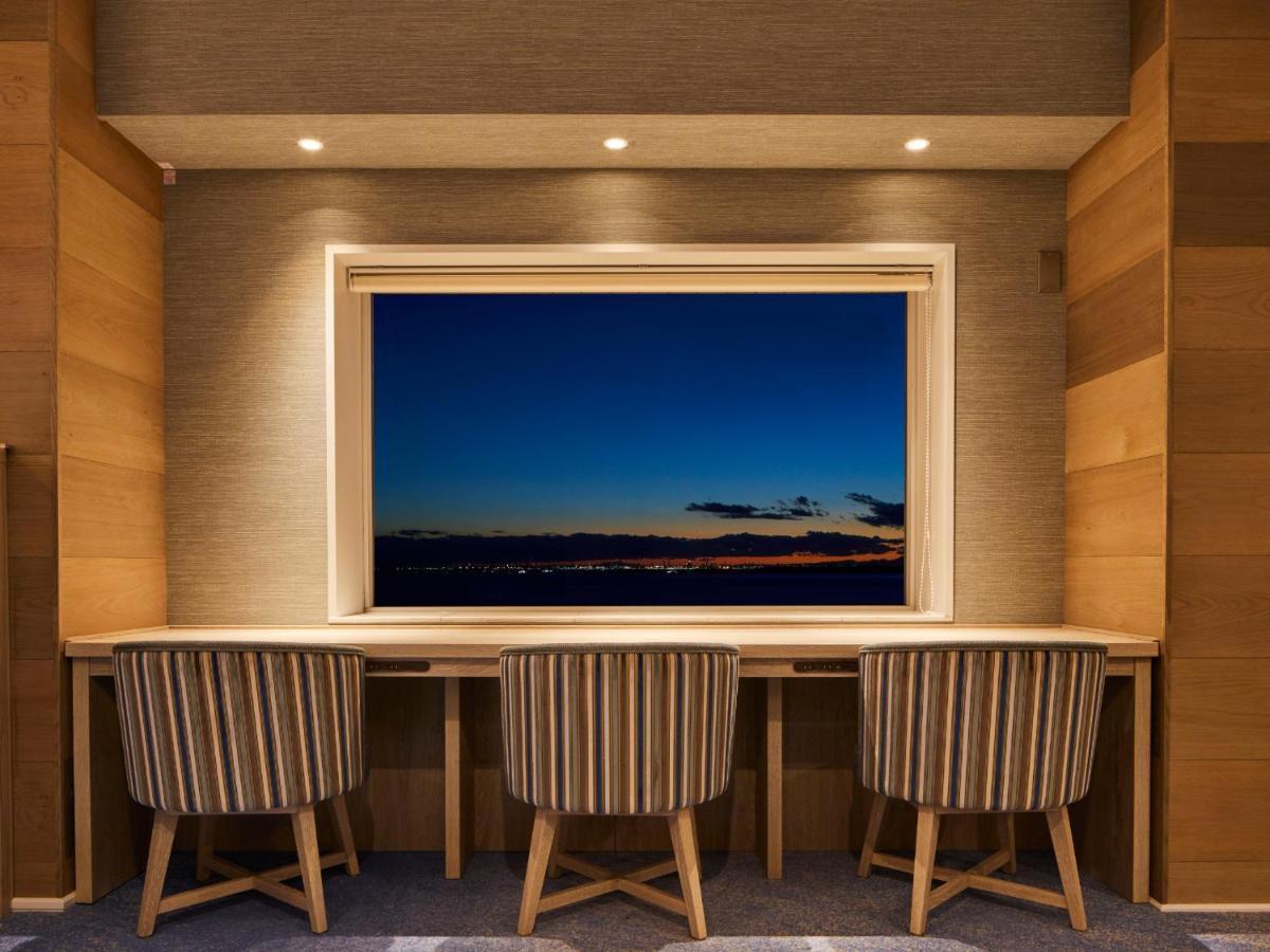 Grand Nikko Tokyo Bay Maihama Hotel Urayasu Eksteriør billede The photo depicts a cozy workspace or study area featuring a long, minimalist desk with three chairs. The wall behind the desk is made of wood, creating a warm atmosphere. At the center, there is a large window that showcases a beautiful evening view