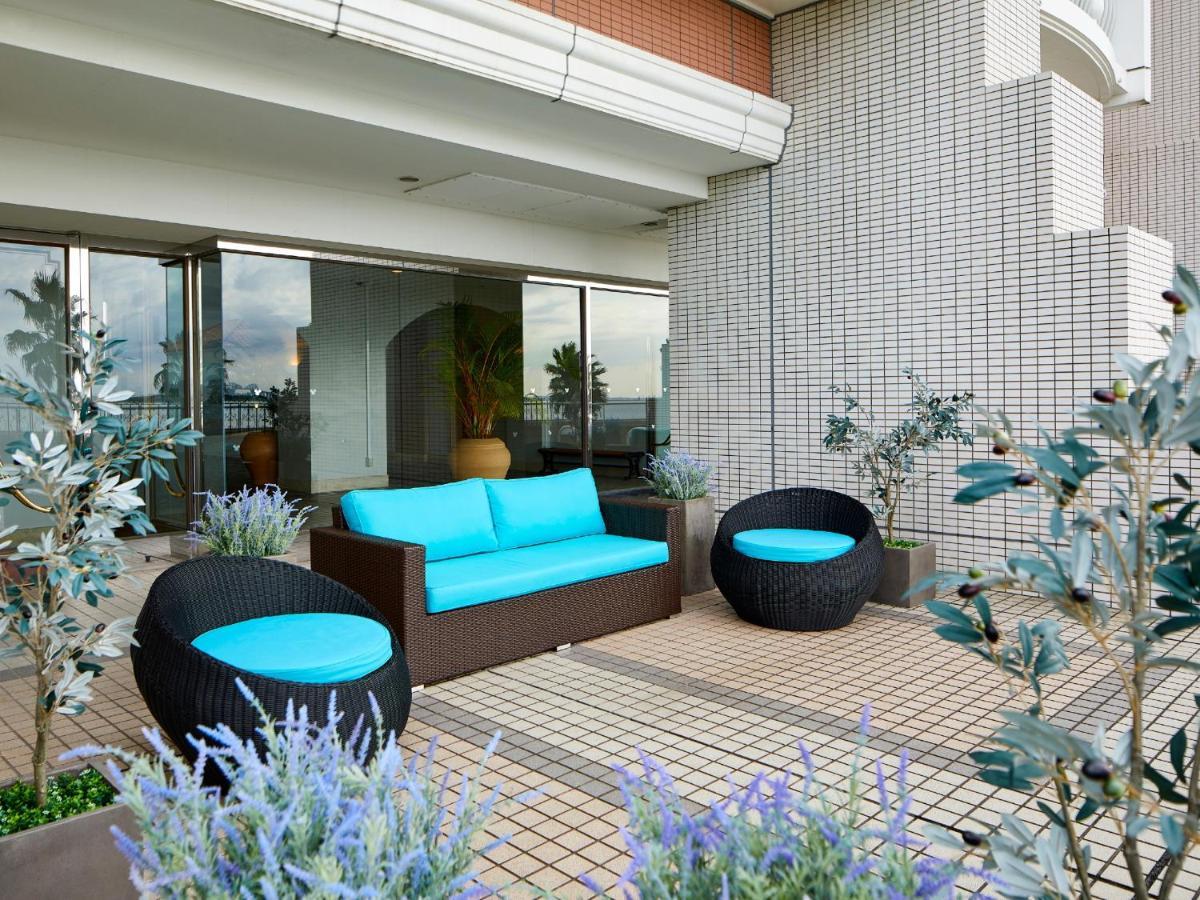 Grand Nikko Tokyo Bay Maihama Hotel Urayasu Eksteriør billede The image shows a stylish outdoor seating area. There is a brown couch with turquoise cushions, complemented by two matching round chairs nearby. The seating is arranged on a tiled patio, which is bordered by planters featuring lavender flowers and g