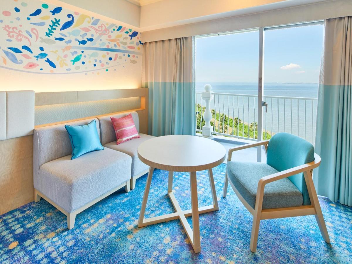 Grand Nikko Tokyo Bay Maihama Hotel Urayasu Eksteriør billede The photo shows a modern and stylish interior of a room with a view. There is a cozy seating area featuring a light-colored sofa with decorative cushions in various shades of blue and pink. A round table occupies the center of the space, surrounded b