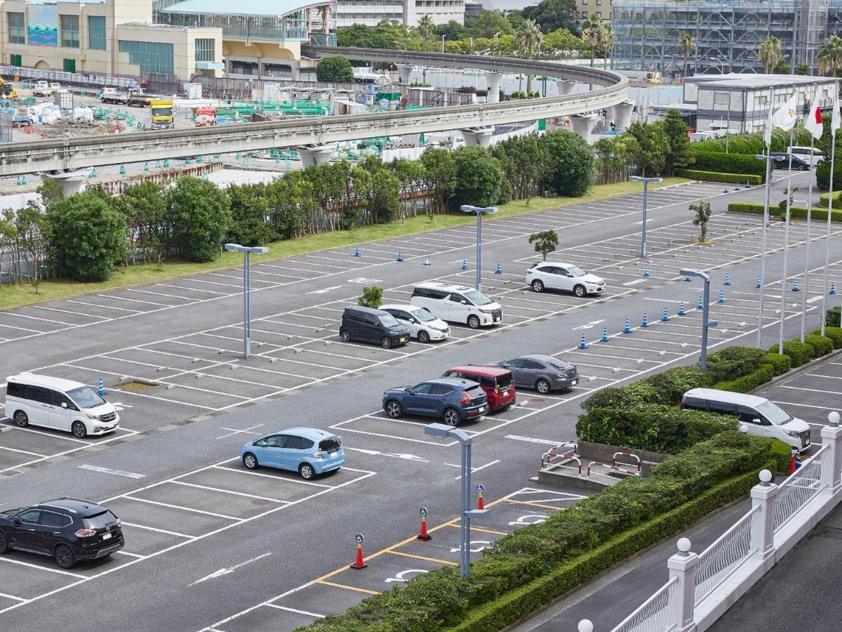 Grand Nikko Tokyo Bay Maihama Hotel Urayasu Eksteriør billede The photo shows a partially empty parking lot with several parked cars. In the foreground, there are a few vehicles, including a blue car and a white one. The lot has clearly marked parking spaces, and there are some trees and shrubs along the sides.
