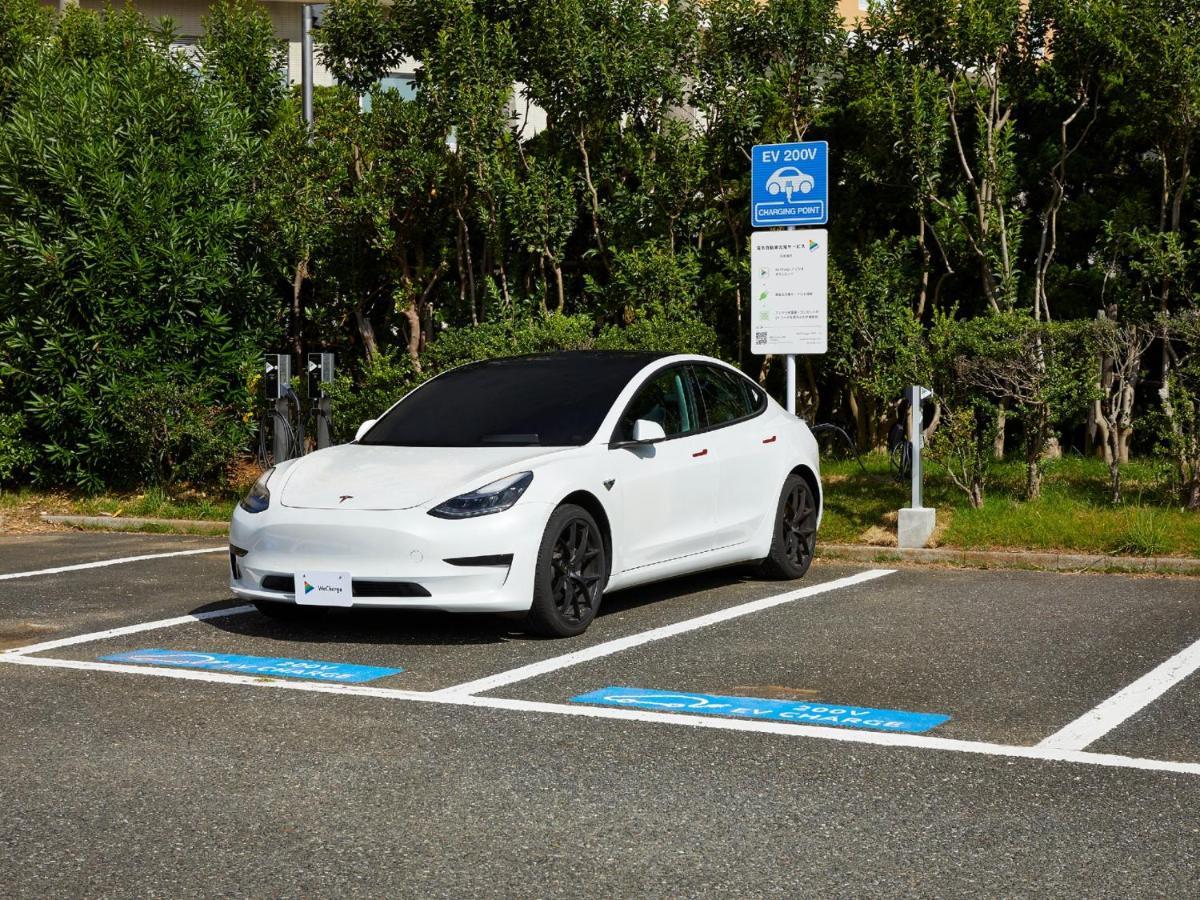 Grand Nikko Tokyo Bay Maihama Hotel Urayasu Eksteriør billede The photo shows a white electric car parked in an EV (electric vehicle) charging spot. The car has a sleek design with black wheels and tinted windows. In the background, there are green shrubs and trees, indicating a natural or landscaped environmen