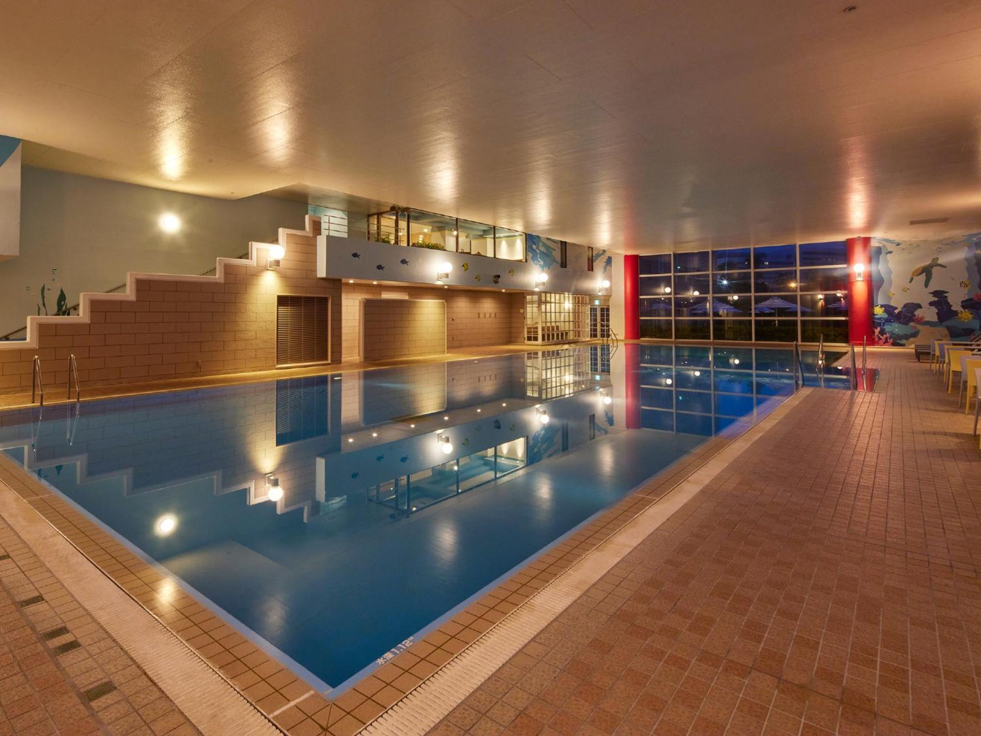 Grand Nikko Tokyo Bay Maihama Hotel Urayasu Eksteriør billede The photo shows an indoor swimming pool area. The pool features a calm blue water surface and is surrounded by tiled flooring. There is a staircase leading to a higher level, likely providing access to a lounge or seating area. Large windows allow na
